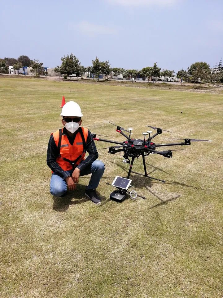 Participante con casco y chaleco junto a un dron multicóptero listo para volar